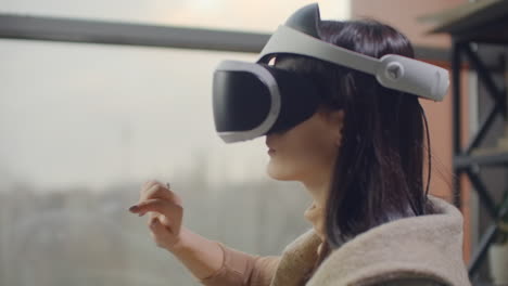 Frau-In-Einem-Helm-Der-Virtuellen-Realität-Vor-Dem-Hintergrund-Eines-Riesigen-Fensters-Im-Büro-Am-Arbeitsplatz.-Architekt,-Der-In-Einem-Virtual-Reality-Helm-Arbeitet.